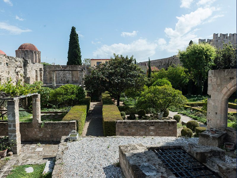 Historic stone garden within a fortress, with trimmed hedges, stone arches, and blue sky above.