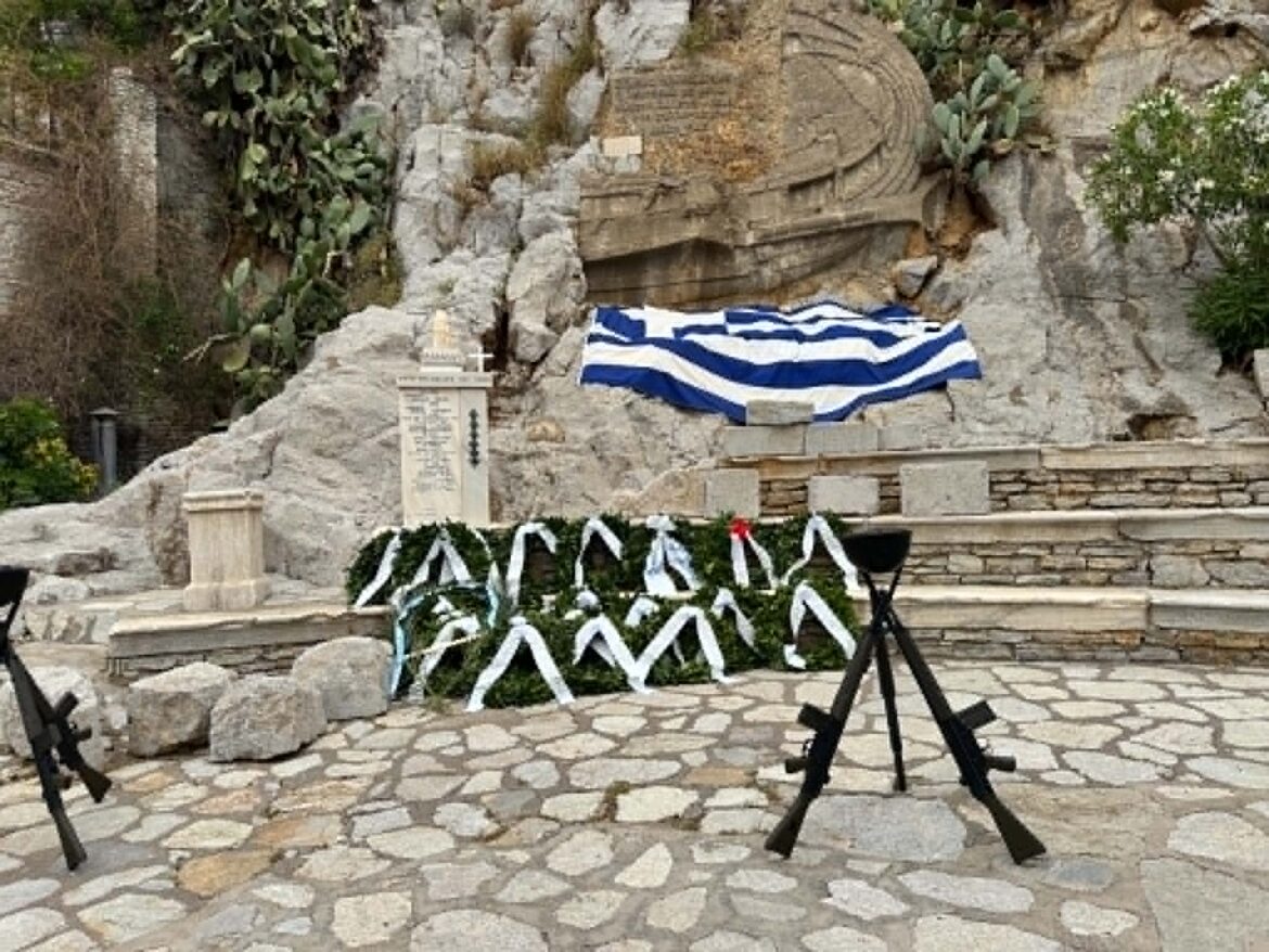 Rocky memorial shrine with a blue-and-white striped cloth draped over a stone altar, surrounded by wreaths and greenery.