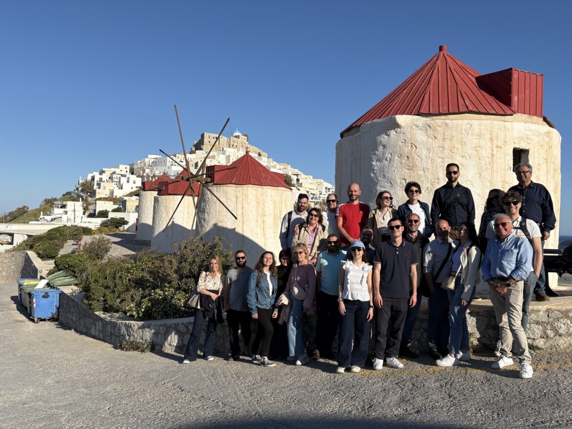 Group of tourists posing in front of traditional windmills on a sunny hillside village.