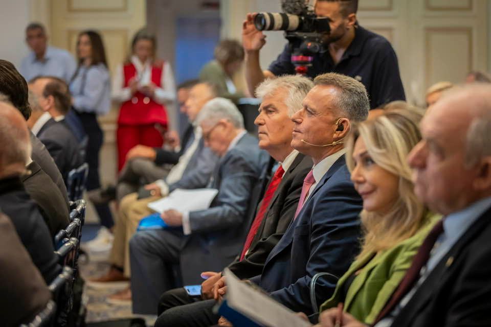 Professionals seated in a conference room, with a photographer filming from the back.