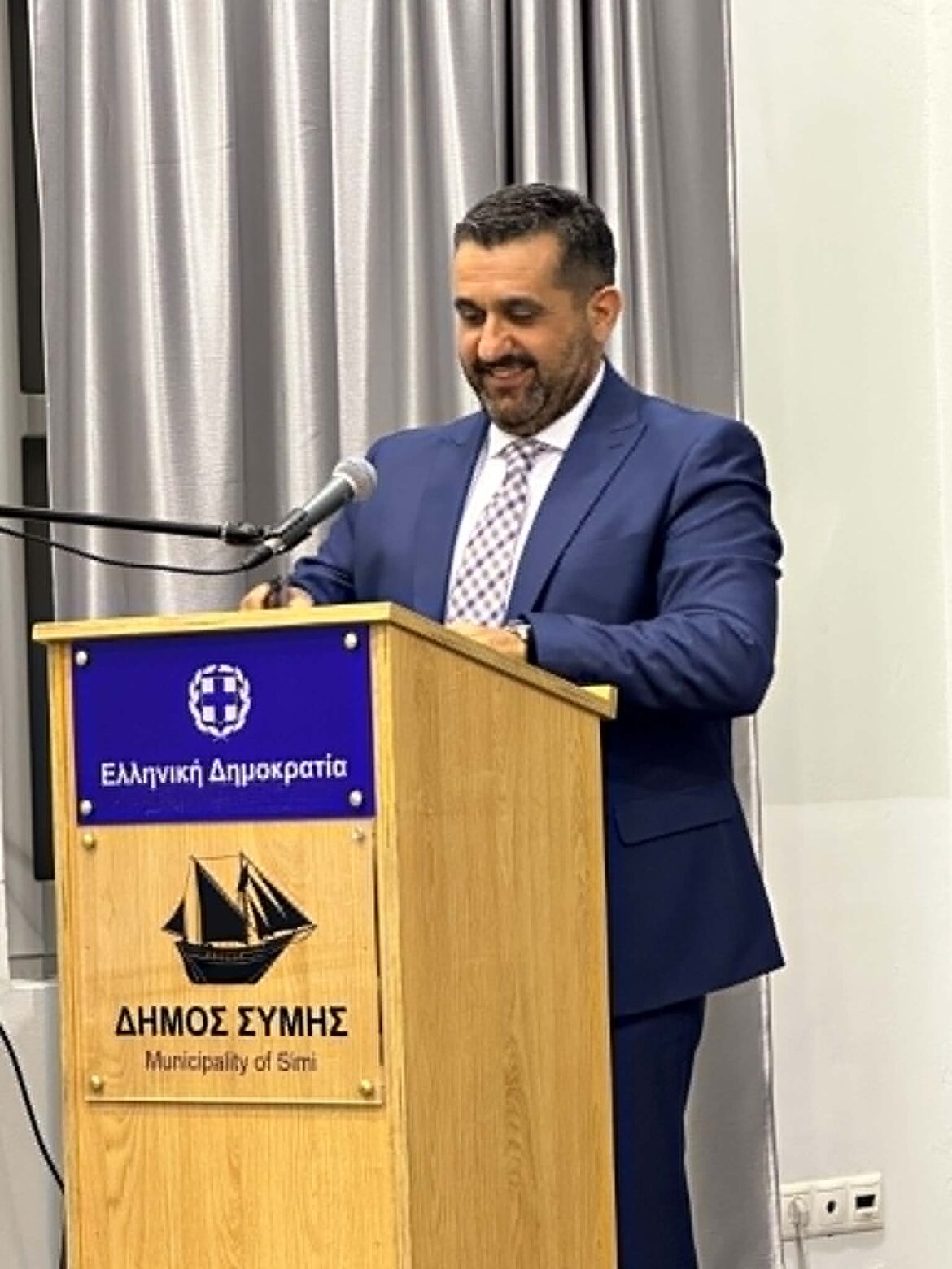Man in a blue suit giving a speech at a wooden podium with a microphone