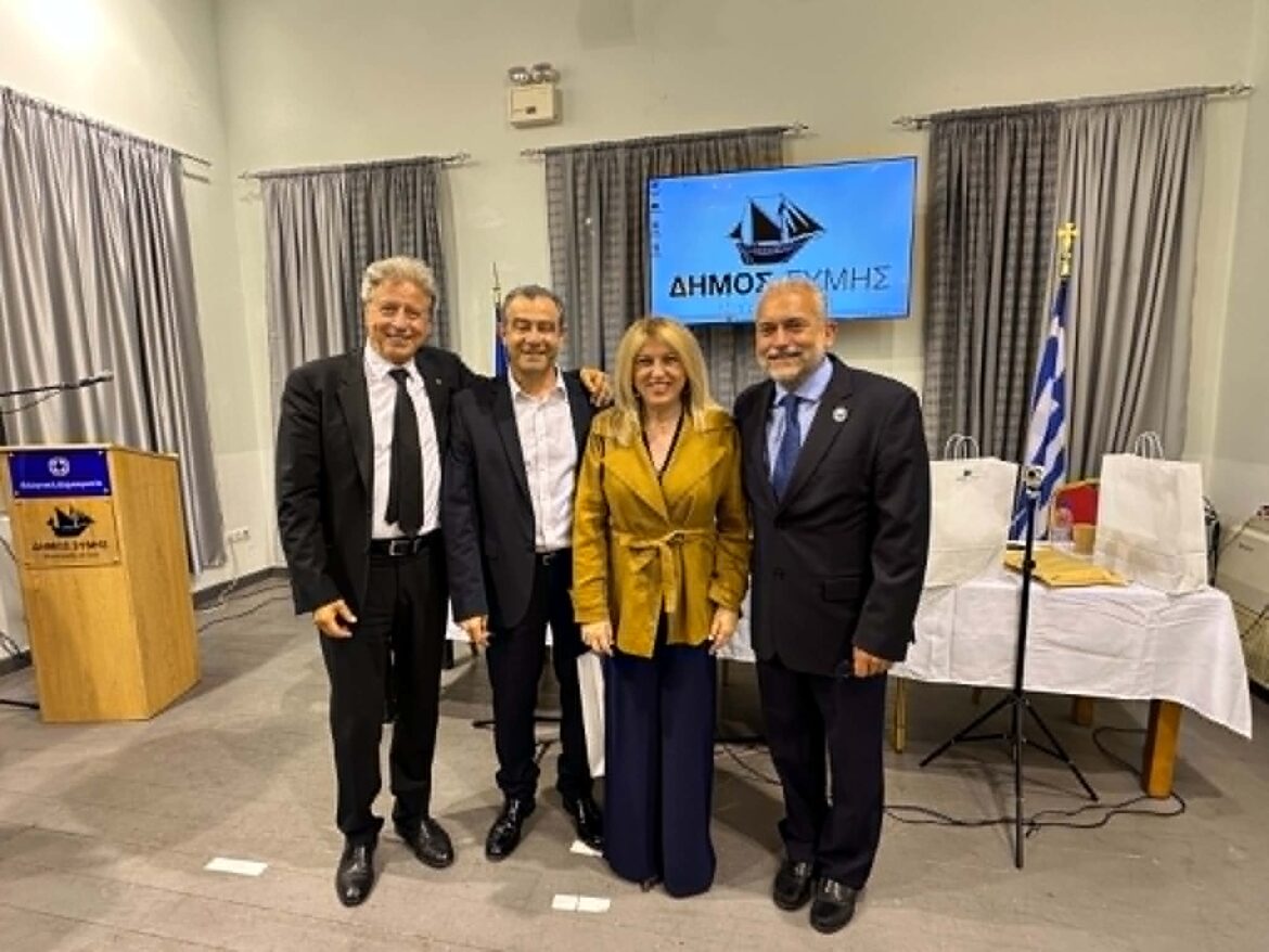 Four professionally dressed adults posing together in a conference room, with a blue municipal banner in the background.