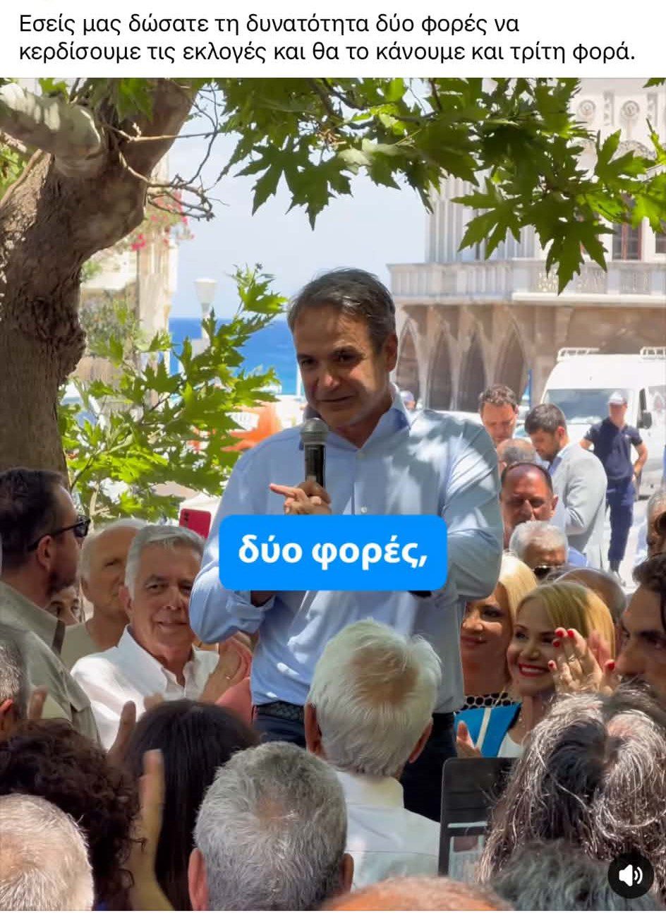Man speaks into a microphone to a crowd at an outdoor rally; Greek caption above and a blue bubble reading 'δύο φορές'.
