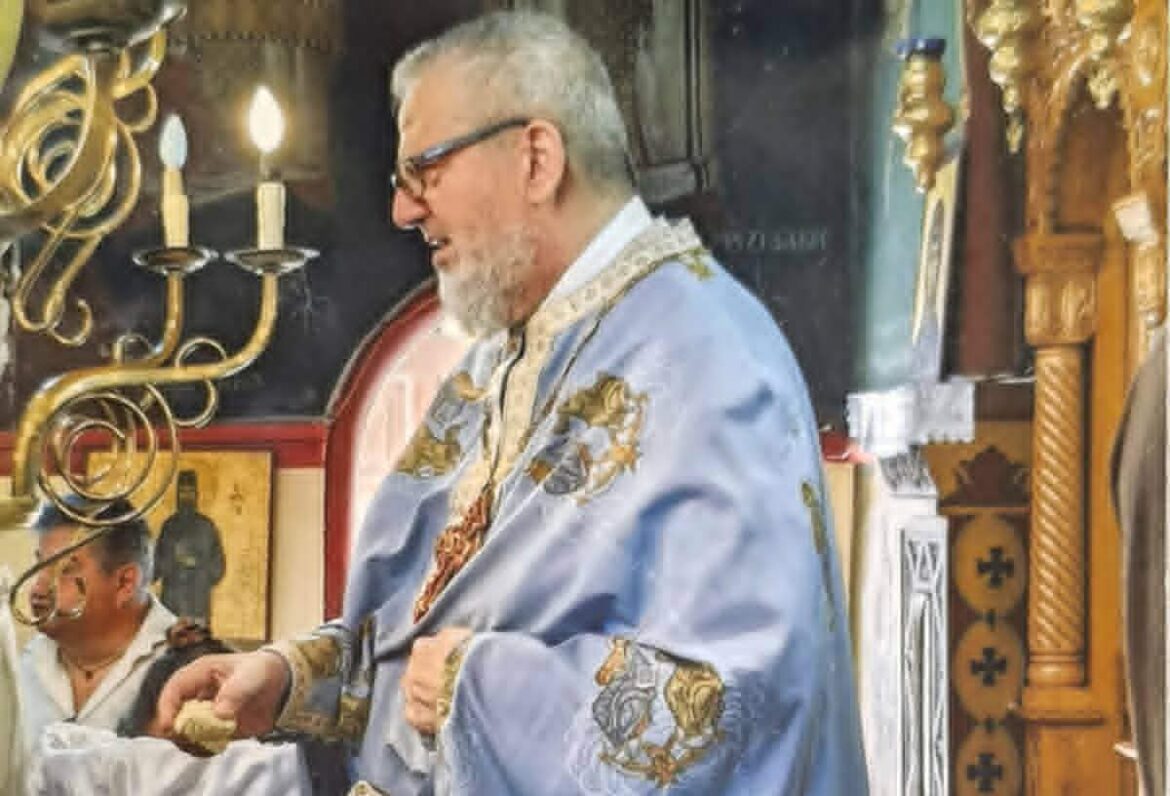 Orthodox priest in blue embroidered vestments giving a blessing inside a church.