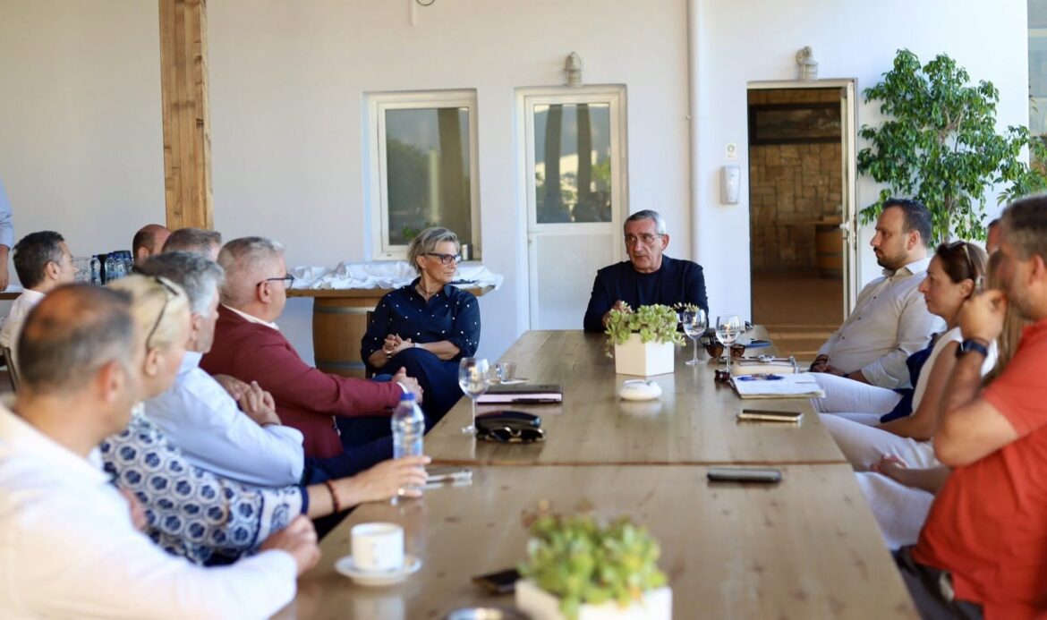 Group of professionals seated around a long wooden table in a sunlit room, with a man and woman at the center leading the discussion.