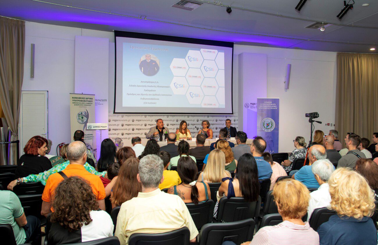 Panel discussion with five speakers at a long table, audience watching, projection screen behind them, banners on sides.