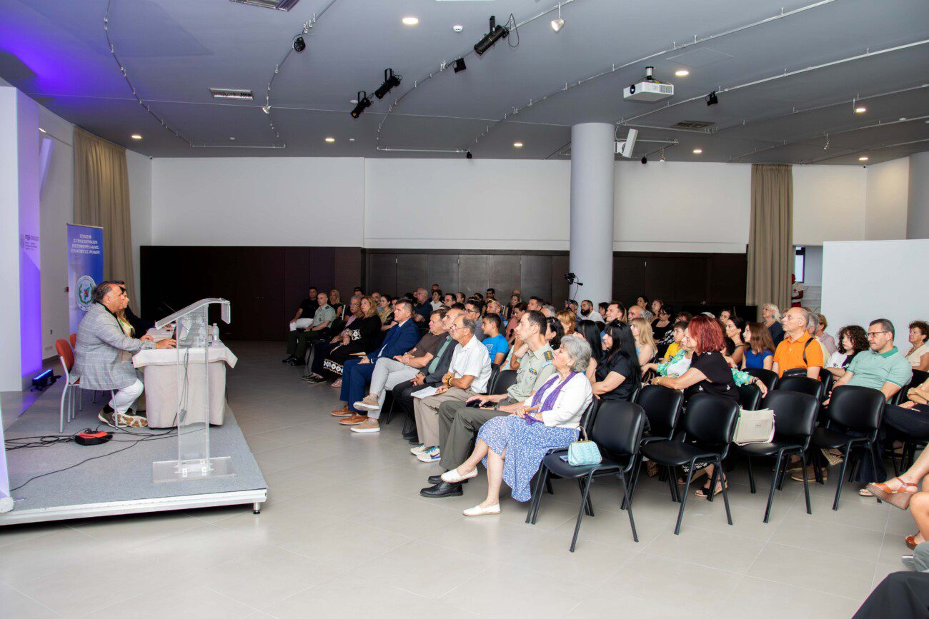 Speaker at a clear podium addressing a conference audience in a modern event hall with rows of attendees seated attentively behind him.