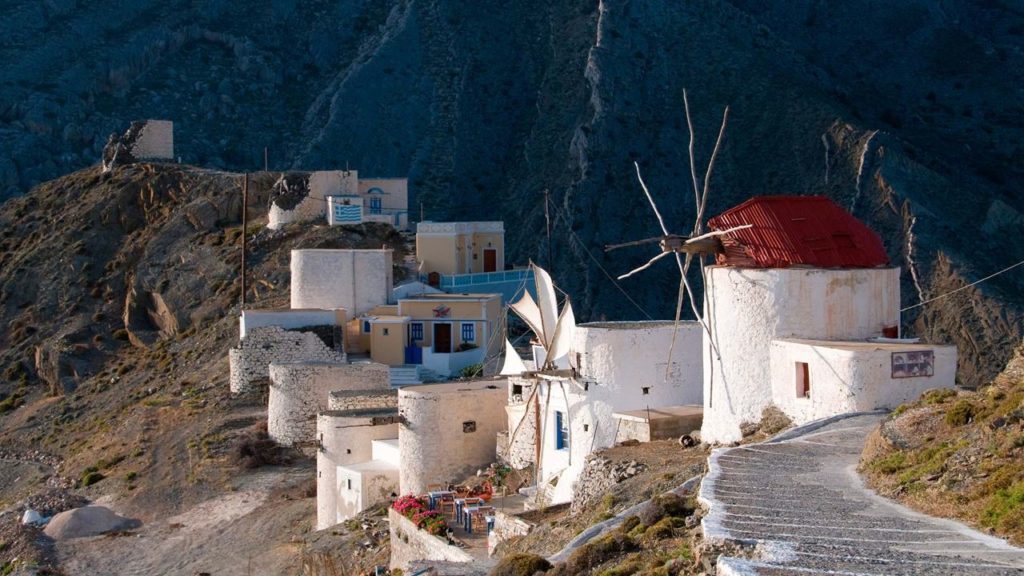 White-washed hillside village with cubic houses and a windmill on a rocky slope.