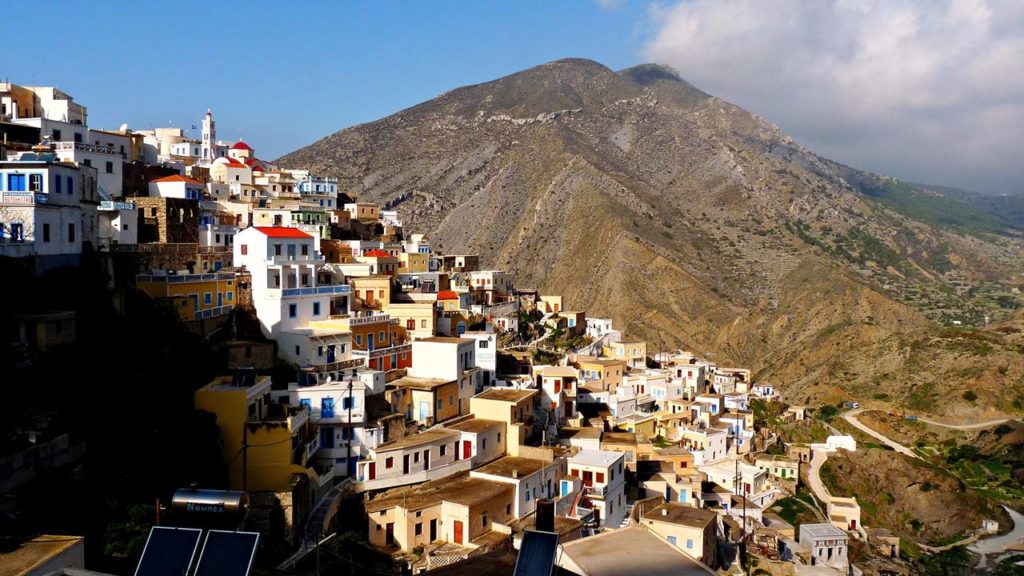 Colorful hillside village built on a steep slope with white and pastel houses against a rocky mountain backdrop