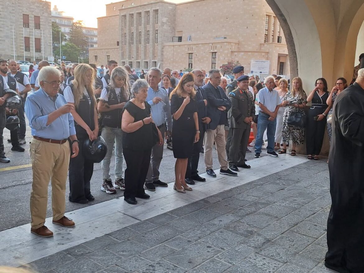 Crowd of adults lined up outside a stone building, some in uniforms, standing solemnly for a formal ceremony under an arched walkway.