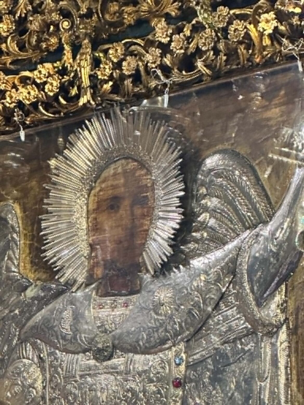 Close-up of ornate gold embroidery and sunburst ornament on a religious statue or vestment, with small colored beads along the edge.