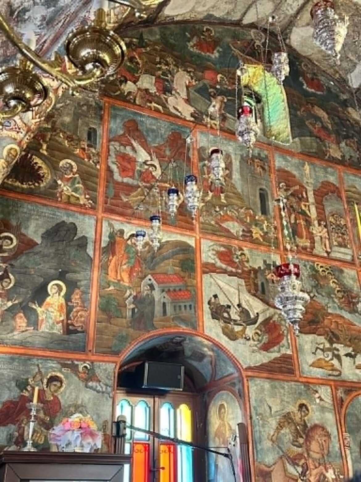 Intricately painted church interior with frescoed panels and ornate gold detailing along the ceiling edge.